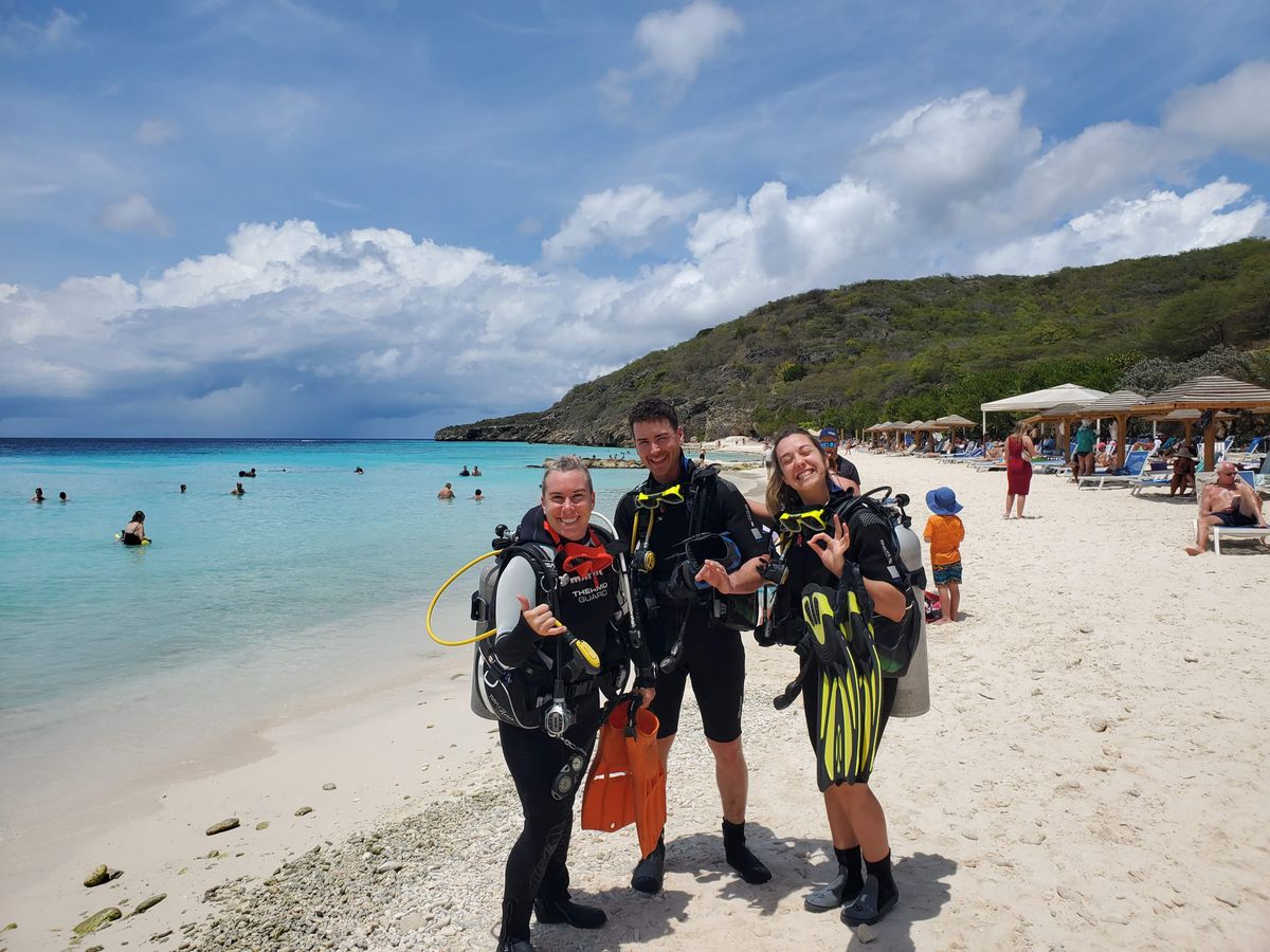 Trois plongeurs équipés posent sur la plage avant la mise à l'eau, à Curaçao.