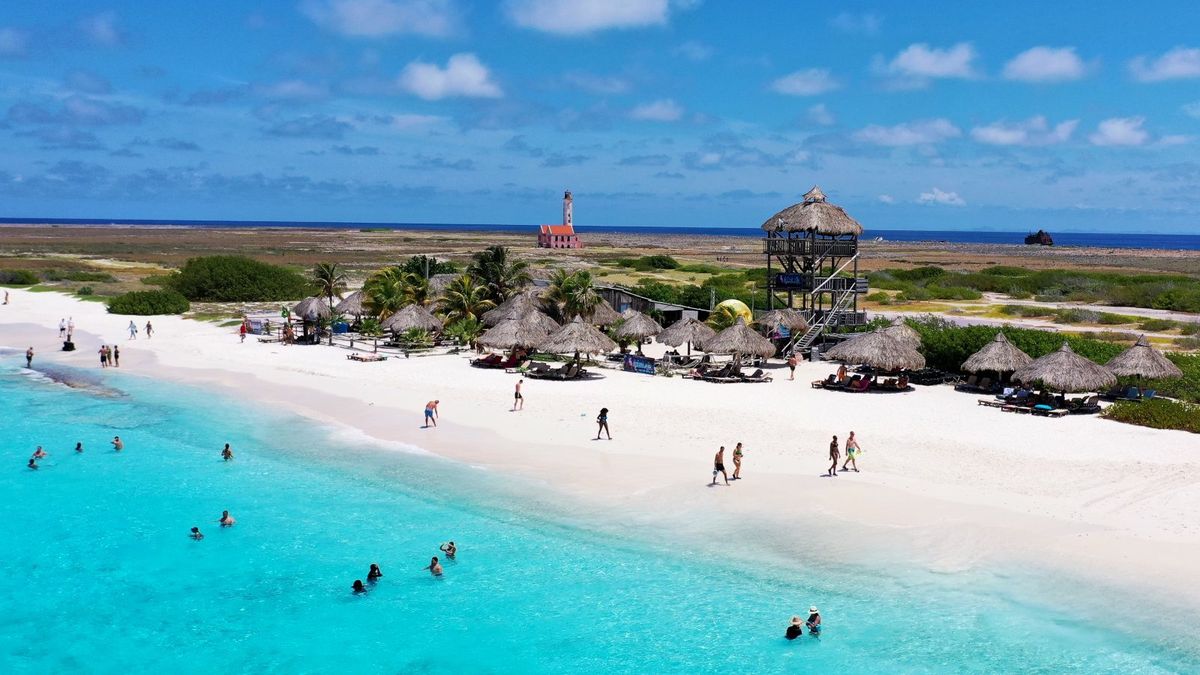 Vue aérienne du phare et des paillotes de Klein Curaçao bordées d'eau turquoise.