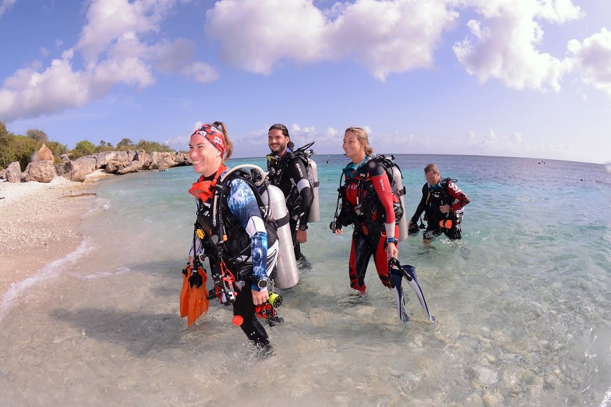Groupe de plongeurs entrant dans l'eau depuis la plage, plongée guidée à Curaçao.