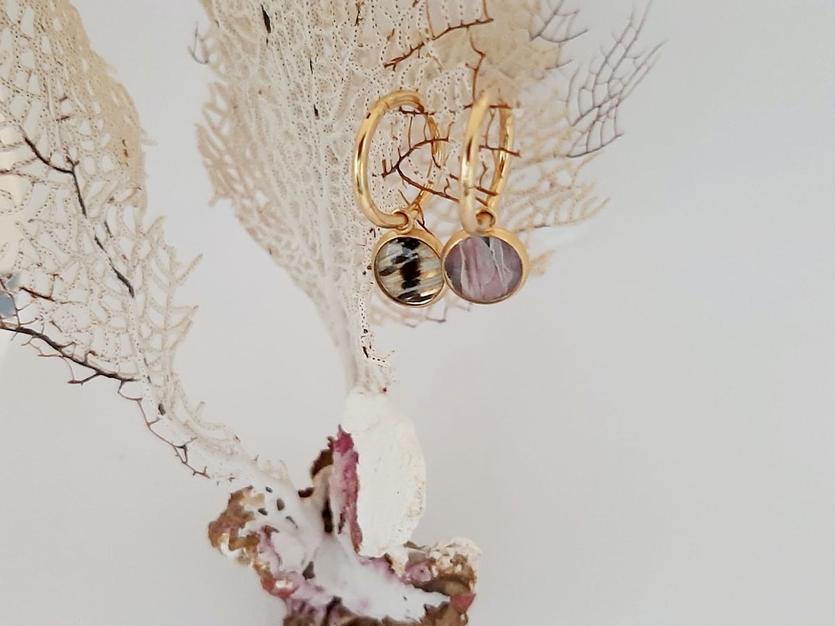 Boucles d'oreilles dorées en nageoire de poisson-lion posées sur un corail blanc.