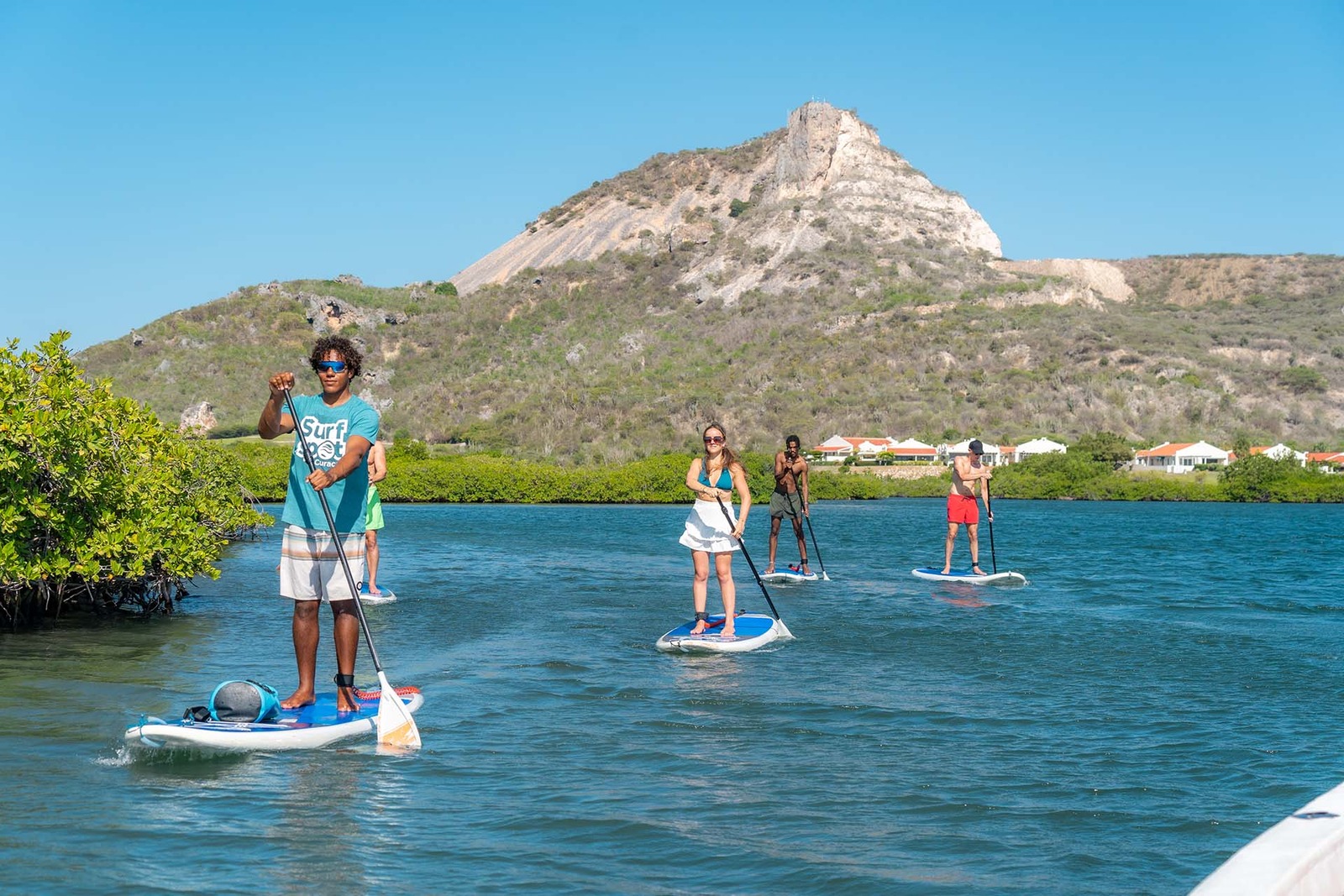 Guide et participantes en paddle board devant une colline rocheuse, Curaçao.