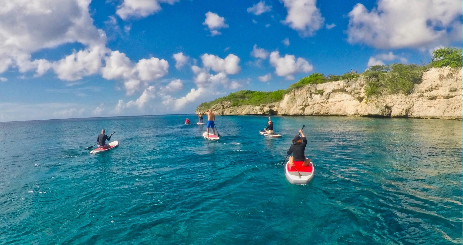 Paddleurs longeant une falaise calcaire dans une eau turquoise, à Curaçao.