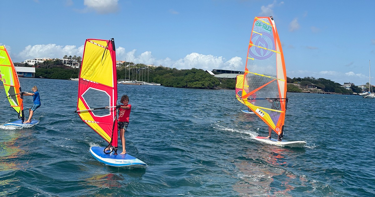 Trois planches à voile aux voiles colorées pendant un cours de groupe à Curaçao.
