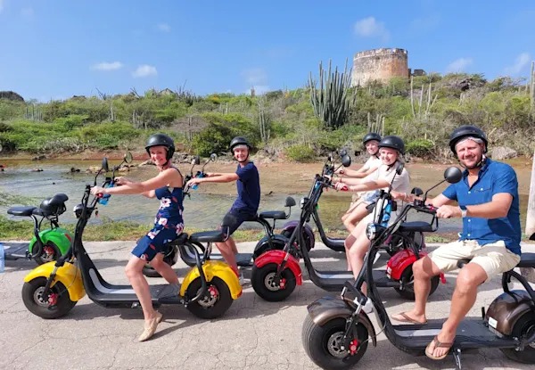 Groupe souriant sur des scooters électriques devant le fort de Caracas Bay, Curaçao.